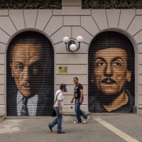 People walk near two murals of the actor, playwrighter and director Eduardo De Filippo realized by the Italian street artist “Jorit” to celebrate the thirtieth anniversary of the great playwrighter’s death in Naples, Italy on October 15, 2014.