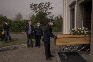 A funeral agency employee carries outiside a church the coffin of a 47 years old man died of coronavirus, while his parents and his wife mourn in the cemetery of Locate Bergamasco, province of Bergamo, Northern Italy on April 16, 2020.