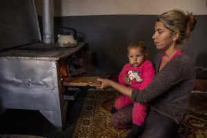 Selma, 18 years old burns wood while holding up her daughter inside her house in the area of Shutka in Skopje, North Macedonia on February 29, 2020. During the winter Selma, like many others households, burns coal, scrap wood, textiles or trash in order to keep warm. This obsolete heating system is one of the biggest contributors to air pollution in the country. Although the electricity tariffs in Macedonia are among the lowest in Europe, energy can cost a third or even half of a citizen’s  average monthly salary. This is the reason why many residents burn wood to heat their home, often buying it on the black market where it costs less, but is more toxic for the environment.