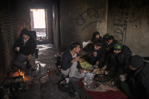 A migrant (left) warms up near a fire while another group of migrants (right) have a breakfast inside an abandoned building in Bihac, Bosnia and Herzegovina on January 27, 2021. Lots of migrants avoid staying inside the Bosnian official refugee camps because of the hard conditions in which they are forced to live and also because the people hosted in the official camps  cannot go out freely.