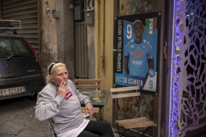 A woman smokes a cigarette near a poster of Napoli footballer Victor Osimhen at the Spanish neighborhoods in Naples, Southern Italy on April 24, 2023.