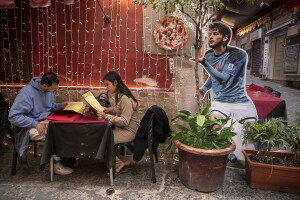 A couple of tourists order a pizza near the giant print of Georgian footballer and Napoli striker Khvicha Kvaratskhelia at Spanish neighborhoods in Naples, Southern Italy on April 3, 2023.