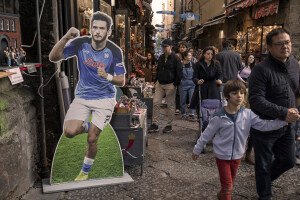 People walk near the giant print of Georgian footballer and Napoli striker Khvicha Kvaratskhelia at San Gregorio Armeno street in Naples, Southern Italy on April 20, 2023.