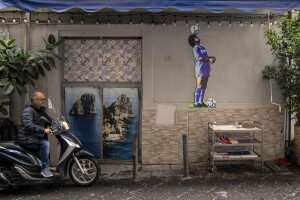 A man is seen near a depiction of Argentine soccer legend Diego Armando Maradona holding a soccer ball at Spanish Quarter in Naples, Southern Italy on November 23, 2021.