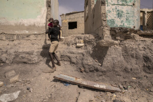 A boy holding a child walks near some houses heavily damaged by the sea in Bargny, Senegal on December 16, 2023. The coastal erosion began in the 1980s but worsened in the early 2000s. Storm surges have become more common and fiercer, like the passage of Hurricane Fred in the night of August 30, 2015. Bargny is currently losing three to four meters of coast each year.