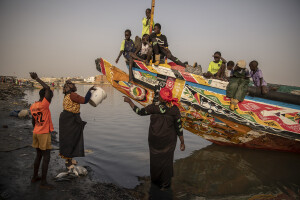 Women and children collect the day’s catch from a pirogue along the coast of the Senegal River in Saint-Louis, Senegal on December 11, 2023. Climate change also affects fishing, a key sector in Senegal which represents 3.2% of the country’s GDP (gross domestic product). The increase in water temperatures is having repercussions on marine ecosystems (changes in the migrations and habits of many fish species) which, in addition to the intensive fishing practiced by foreign fishing boats, is reducing the country’s fish resources. Furthermore, the advance of the sea is forcing many fishermen in Saint-Louis to leave their homes facing the sea and move inland: now to reach the sea and go fishing they have to face long and expensive journeys.