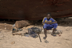 A young fisherman is seen on the beach of Saint-Louis, Senegal on December 14, 2023. Climate change also affects fishing, a key sector in Senegal which represents 3.2% of the country’s GDP (gross domestic product). The increase in water temperatures is having repercussions on marine ecosystems (changes in the migrations and habits of many fish species) which, in addition to the intensive fishing practiced by foreign fishing boats, is reducing the country’s fish resources. Furthermore, the advance of the sea is forcing many fishermen in Saint-Louis to leave their homes facing the sea and move inland: now to reach the sea and go fishing they have to face long and expensive journeys.