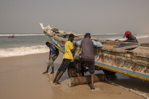 A group of fishermen drags a pirogue into the sea before going fishing in Saint-Louis, Senegal on December 12, 2023. Climate change also affects fishing, a key sector in Senegal which represents 3.2% of the country’s GDP (gross domestic product). The increase in water temperatures is having repercussions on marine ecosystems (changes in the migrations and habits of many fish species) which, in addition to the intensive fishing practiced by foreign fishing boats, is reducing the country’s fish resources. Furthermore, the advance of the sea is forcing many fishermen in Saint-Louis to leave their homes facing the sea and move inland: now to reach the sea and go fishing they have to face long and expensive journeys.