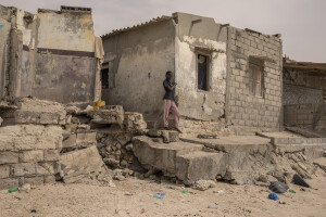 A girl is seen near some houses heavily damaged by sea waves while some children play on the beach in Bargny, Senegal on December 19, 2023. The coastal erosion began in the 1980s but worsened in the early 2000s. Storm surges have become more common and fiercer, like the passage of Hurricane Fred in the night of August 30, 2015. Bargny is currently losing three to four meters of coast each year.