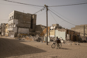 A man drags a bicycle near a demolished house in the “Langue de Barbarie” in Saint-Louis, Senegal on December 12, 2023. The Senegalese government is offering money to families who leave their homes by the sea and move to Djougop temporary camp, and then proceeds to demolish those homes. The “Langue de Barbarie” is a thin, sandy peninsula located in western Senegal, where around 80,000 people live and is among the places most threatened by the rise in sea levels generated by climate change. The peninsula separates the Atlantic ocean from the final section of the Senegal river.