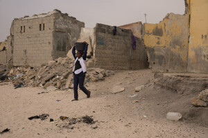 A woman with a basin on her head is seen near some houses heavily damaged by sea waves in Bargny, Senegal on December 19, 2023. The coastal erosion began in the 1980s but worsened in the early 2000s. Storm surges have become more common and fiercer, like the passage of Hurricane Fred in the night of August 30, 2015. Bargny is currently losing three to four meters of coast each year.