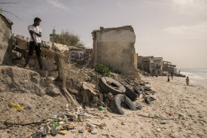 A man is seen near some houses heavily damaged by sea waves while some children play on the beach in Bargny, Senegal on December 16, 2023. The coastal erosion began in the 1980s but worsened in the early 2000s. Storm surges have become more common and fiercer, like the passage of Hurricane Fred in the night of August 30, 2015. Bargny is currently losing three to four meters of coast each year.